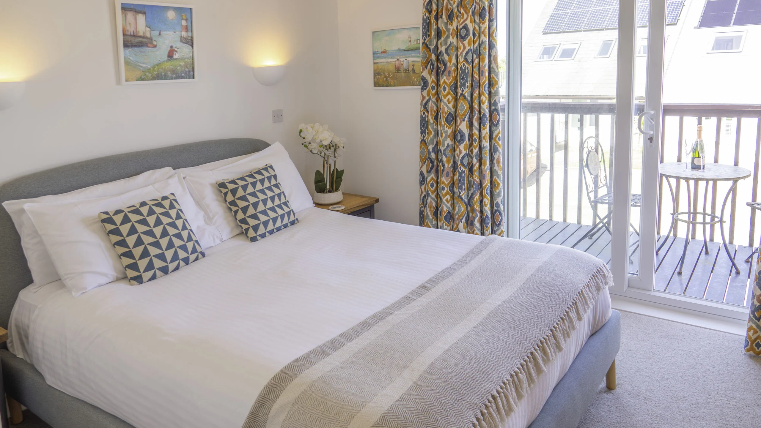 Villa 12a bedroom. Double bed with bedside table. Sliding doors leading out to the balcony. Balcony is furnished with two chairs and a table.